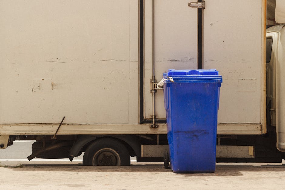 A large amount of mixed household waste, including black plastic garbage bags, cardboard boxes, and discarded items, is piled up on the pavement outside a property. The garbage bags are scattered amon